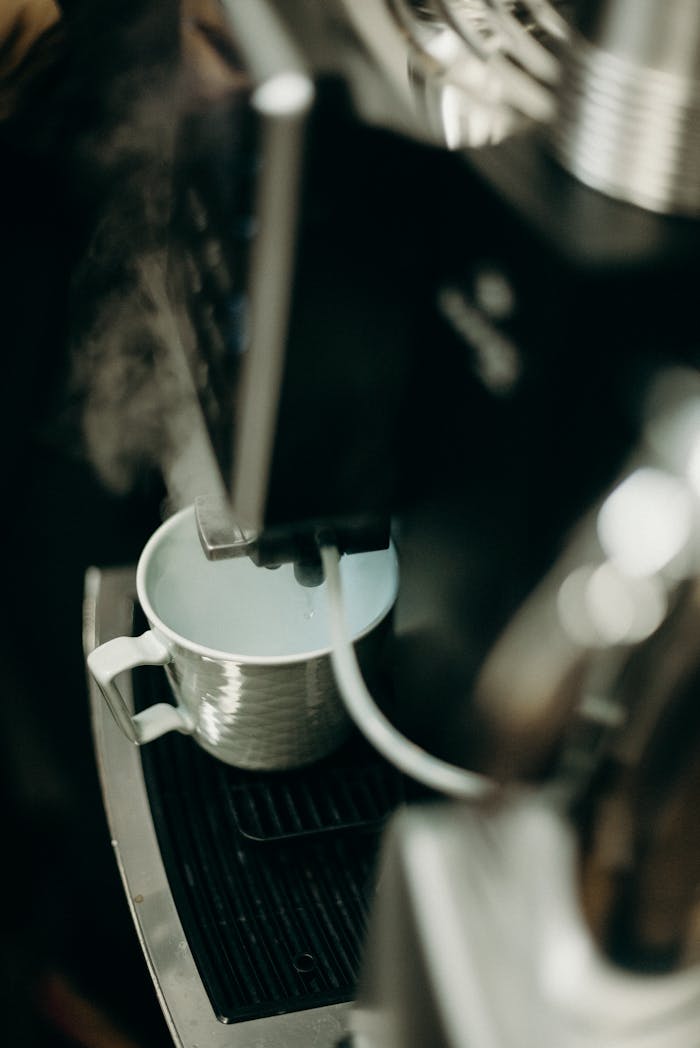 A steaming cup being filled under an espresso machine, captured in warm tones and selective focus.