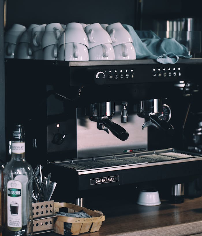 A commercial espresso machine surrounded by stacked white cups in a cozy coffee shop setting.