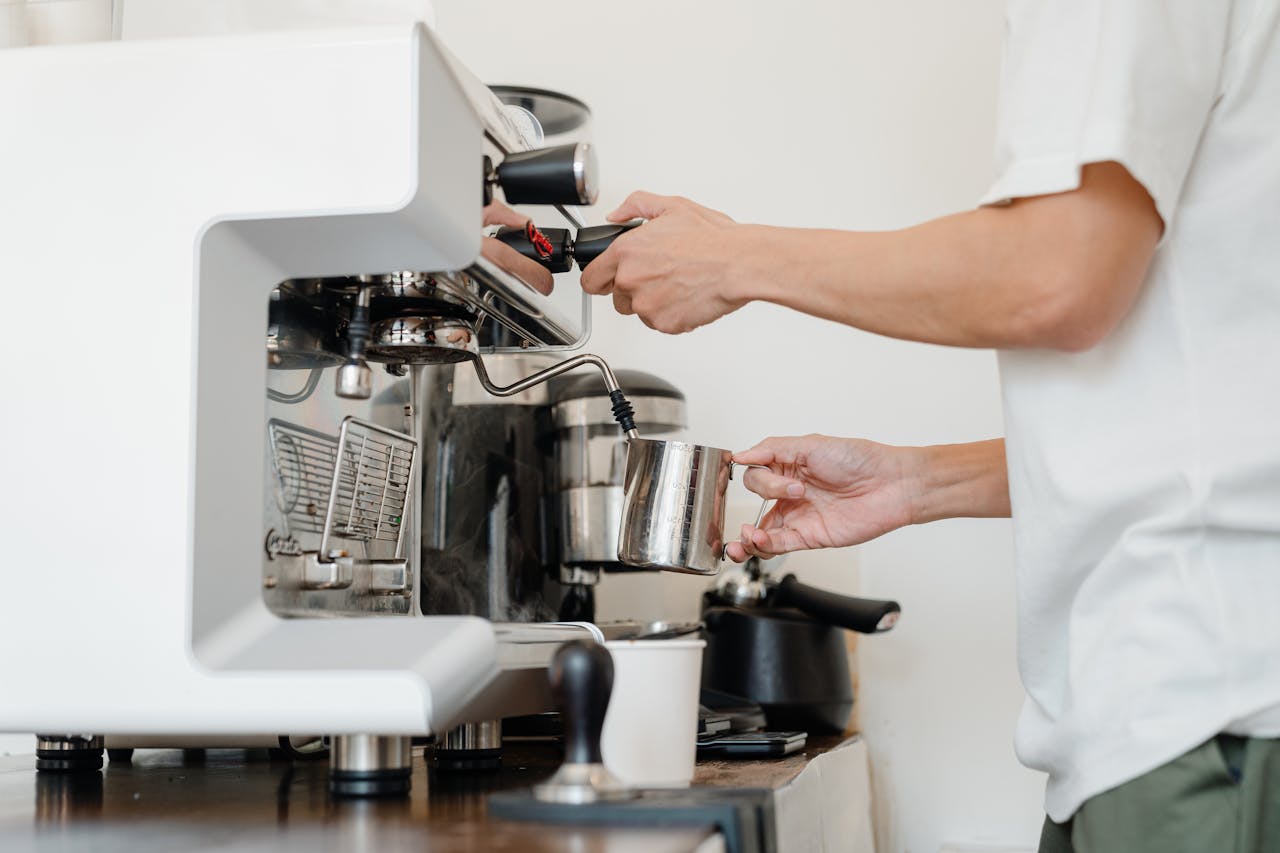 Close-up of a barista steaming milk using an espresso machine in a cafe setting.